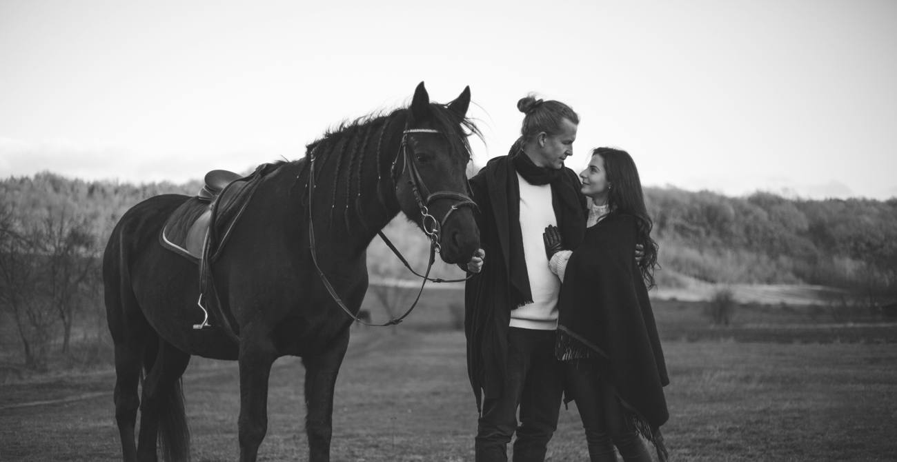 Un couple se regarde à côté d'un cheval, en noir et blanc